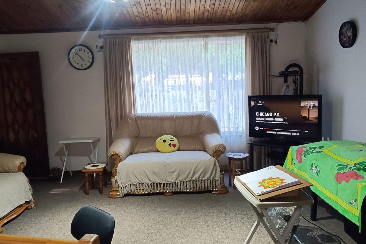 A living room featuring a timber-clad ceiling, carpeted flooring, and a large window providing natural light.