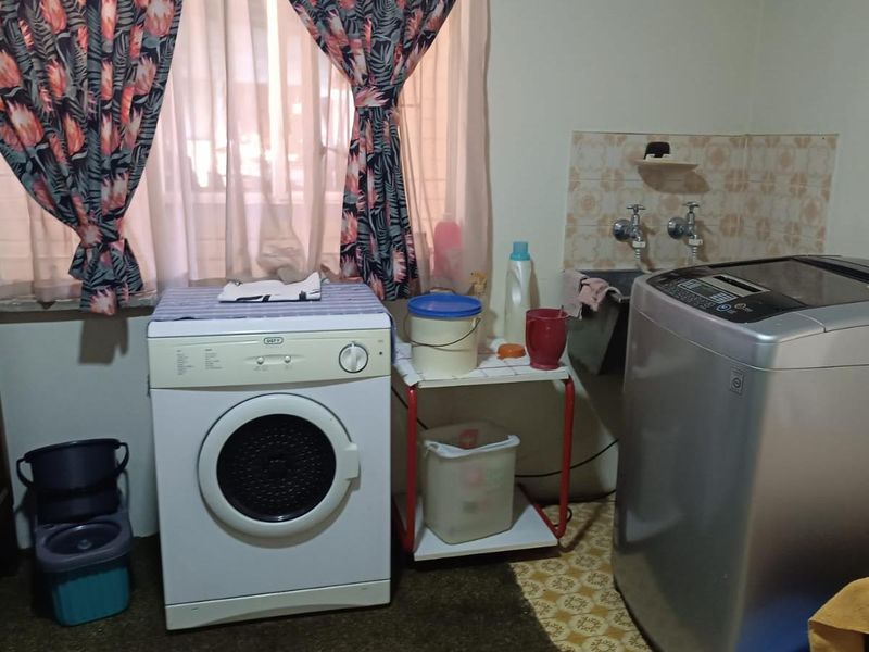 A functional laundry area featuring a utility sink, tiled splashback, and space for multiple washing appliances.