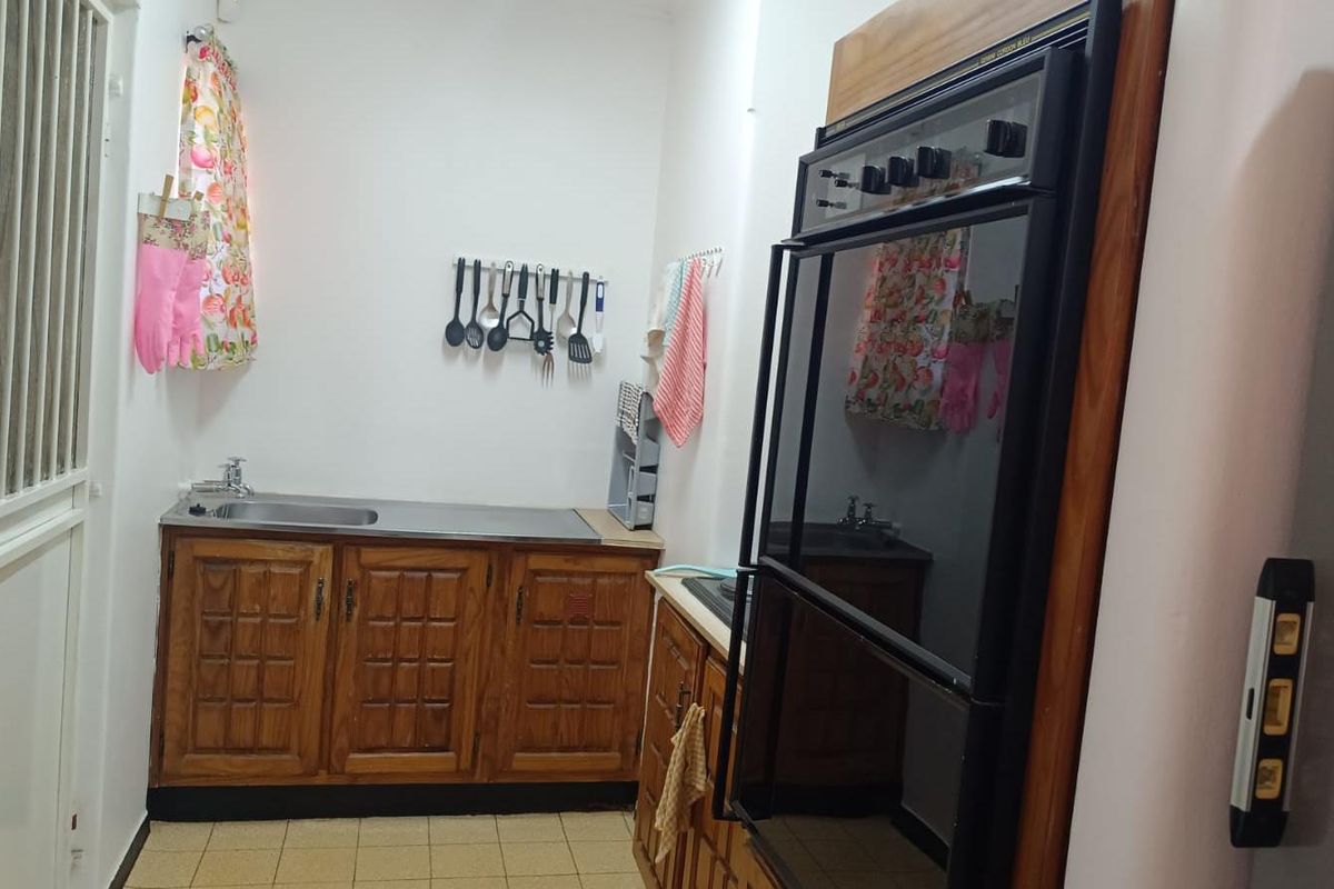 A compact kitchen featuring dated wooden cabinetry, a built-in double oven, and a stainless steel sink with tiled flooring.