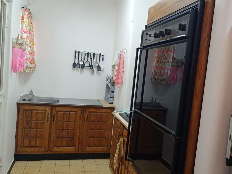 A compact kitchen featuring dated wooden cabinetry, a built-in double oven, and a stainless steel sink with tiled flooring.