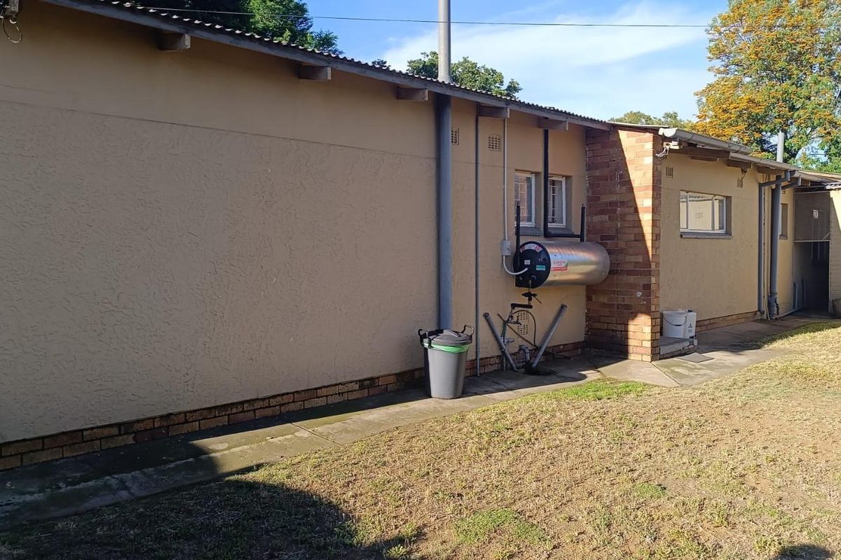 Rear exterior view of the property featuring a brick and plaster facade, external geyser, and concrete pathway along the building perimeter.