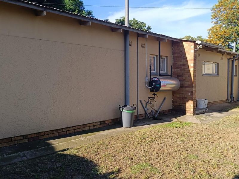 Rear exterior view of the property featuring a brick and plaster facade, external geyser, and concrete pathway along the building perimeter.