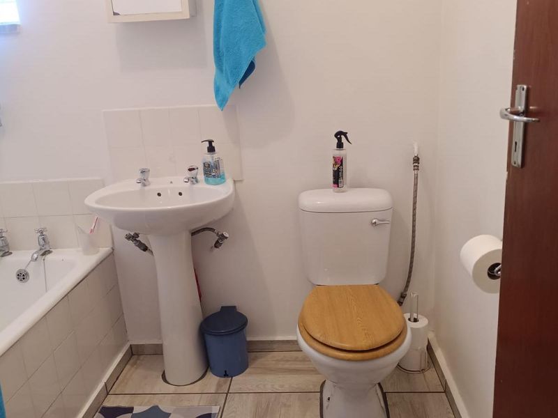 A functional bathroom featuring a pedestal basin, standard bathtub, and toilet with tiled flooring and splashback finishes.