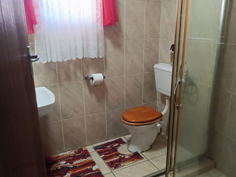 A functional bathroom featuring a shower enclosure, toilet, and washbasin with neutral wall and floor tiling.