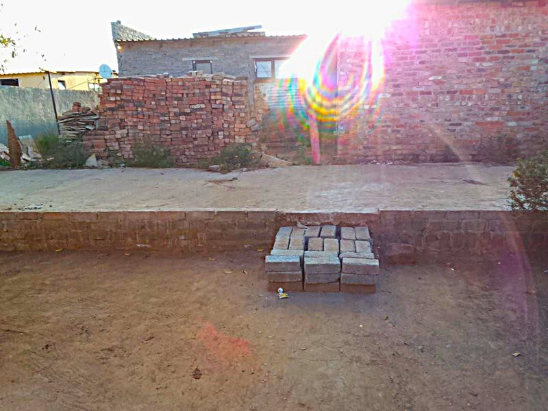 Rear exterior view of a property featuring unfinished brick masonry walls and a concrete patio area in need of landscaping and completion.