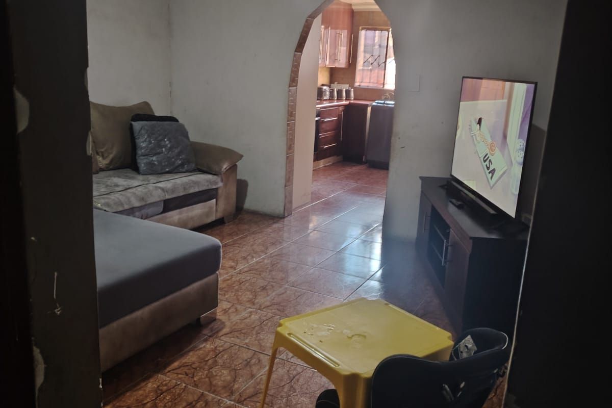 A living room featuring tiled flooring and an arched entryway leading to the kitchen, currently requiring wall repairs and cosmetic updates.