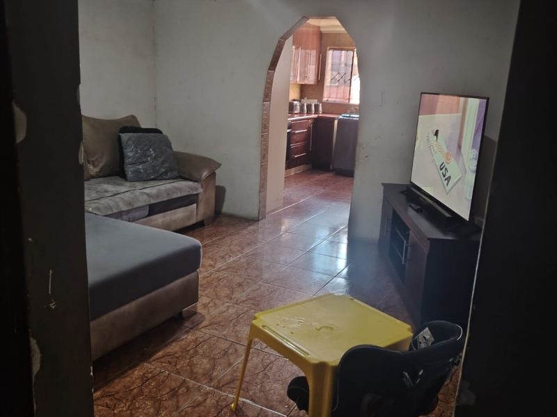 A living room featuring tiled flooring and an arched entryway leading to the kitchen, currently requiring wall repairs and cosmetic updates.