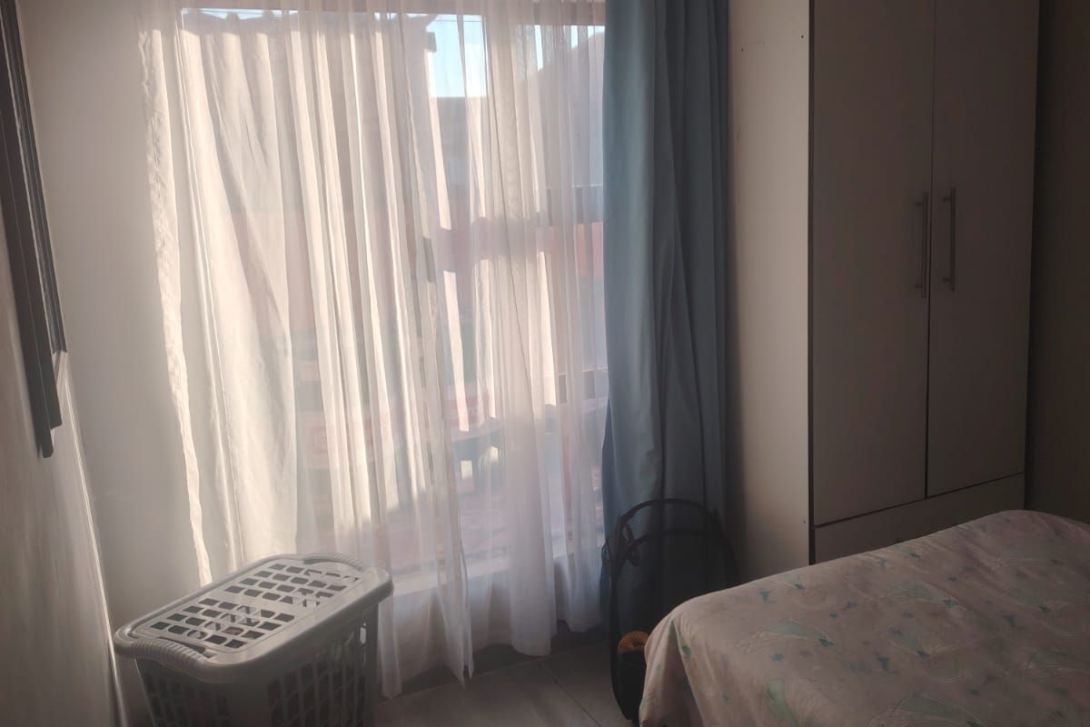 A bedroom featuring tiled flooring and a built-in wardrobe, with natural light entering through a window.