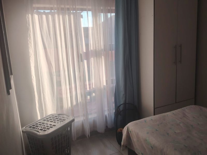 A bedroom featuring tiled flooring and a built-in wardrobe, with natural light entering through a window.