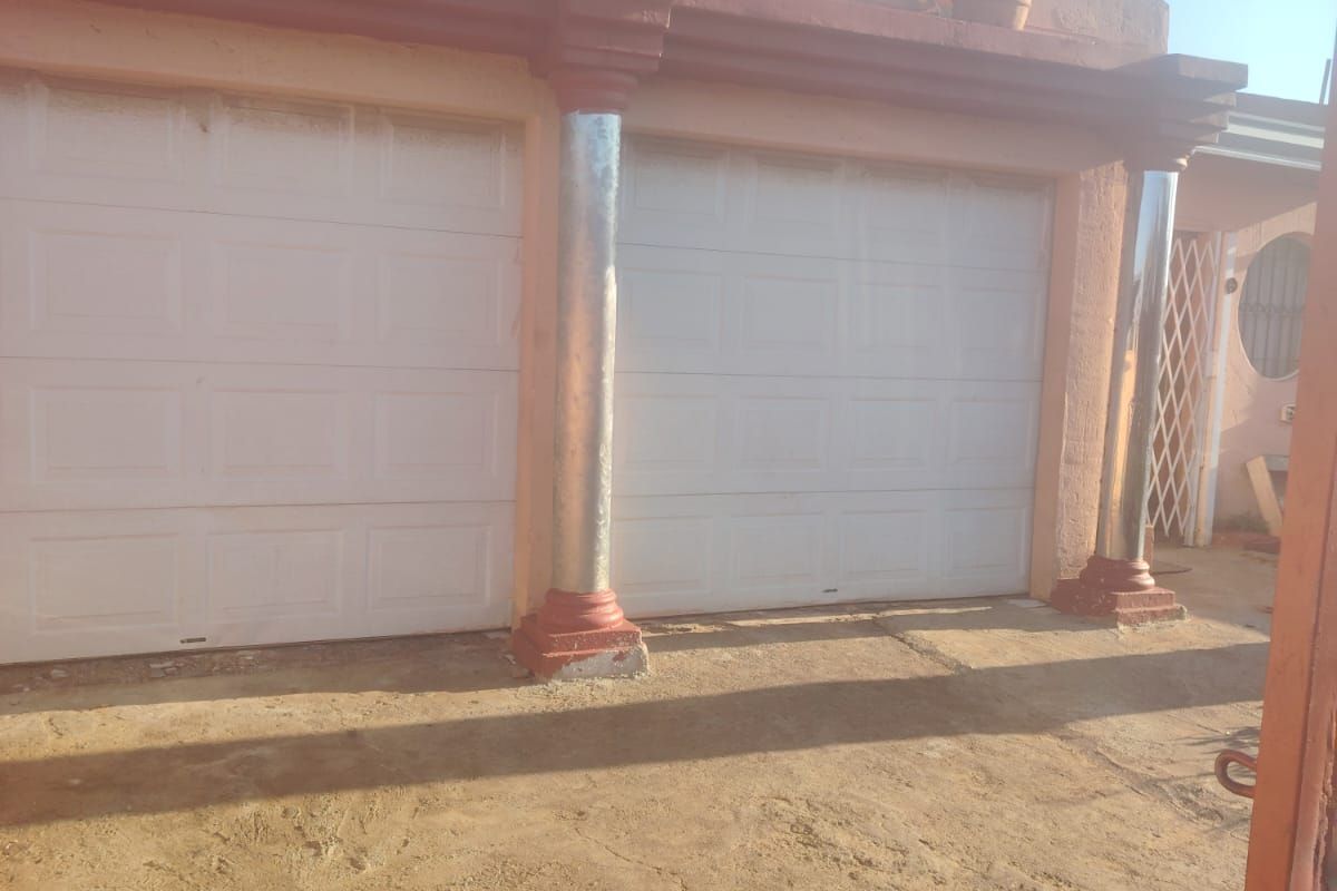 Exterior view of a double garage featuring white sectional doors and decorative columns, set against a concrete driveway area.