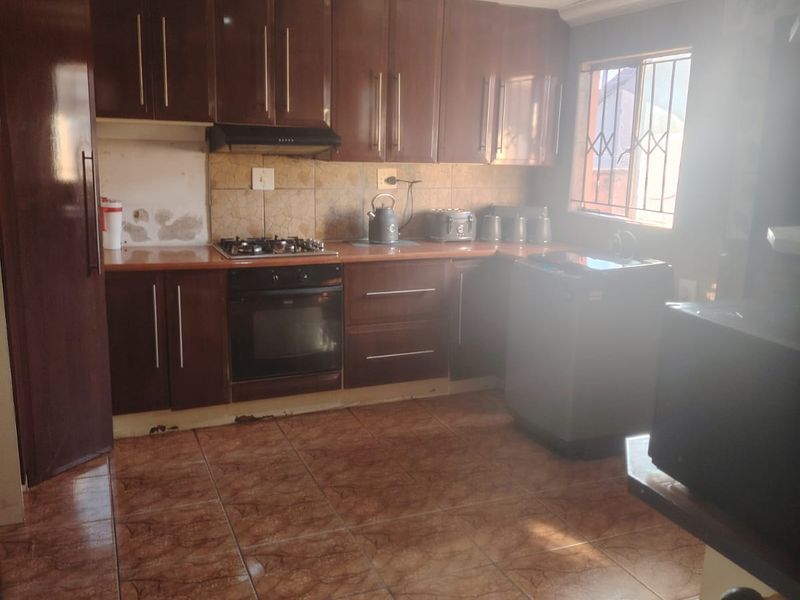 A functional kitchen featuring dark wood cabinetry, tiled flooring, a gas hob, and built-in oven, with some visible wear to the cabinetry and wall finishes.