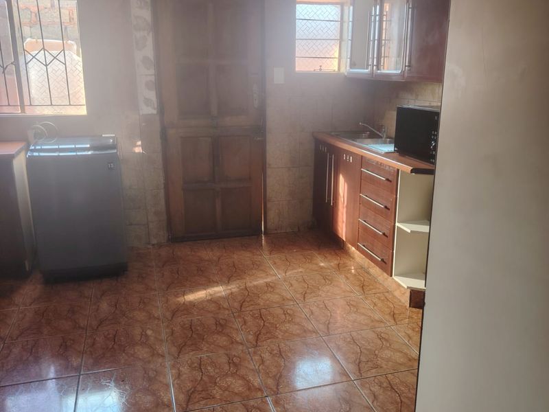 A functional kitchen area featuring tiled flooring, built-in cabinetry, and direct exterior access through a wooden door.