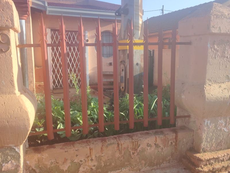 Front exterior view of the property featuring a masonry boundary wall with metal security fencing and a security gate at the entrance.