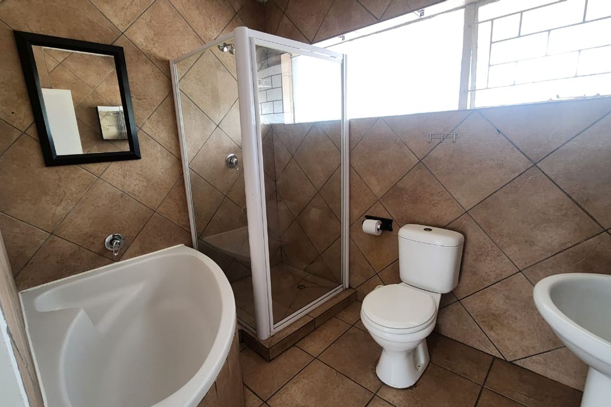 A functional bathroom featuring a corner bathtub, separate shower enclosure, pedestal basin, and toilet, finished with neutral wall and floor tiling.