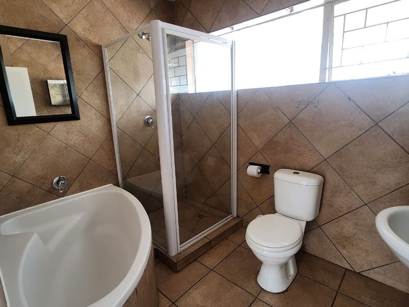A functional bathroom featuring a corner bathtub, separate shower enclosure, pedestal basin, and toilet, finished with neutral wall and floor tiling.