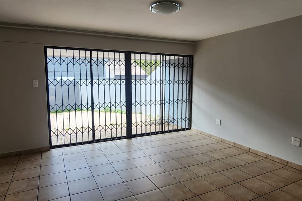 An empty living room featuring tiled flooring and a large sliding security gate providing access to the outdoor area.