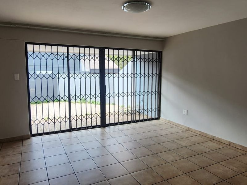 An empty living room featuring tiled flooring and a large sliding security gate providing access to the outdoor area.