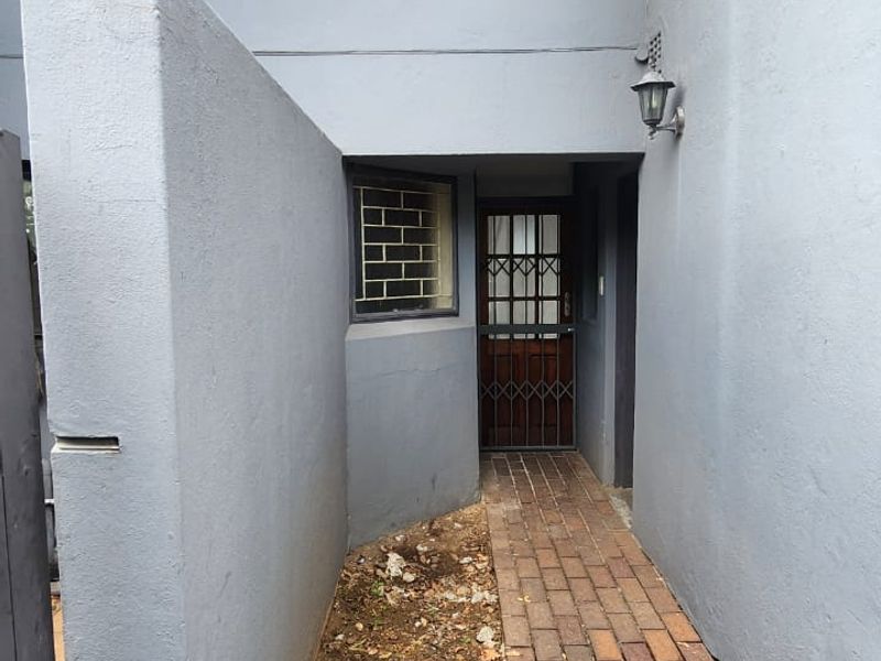A private entrance walkway featuring brick paving, a security gate, and an exterior wall light, leading to the main front door.