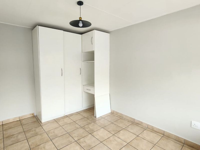 A bright, empty bedroom featuring neutral walls, tiled flooring, and a white built-in wardrobe with integrated shelving.