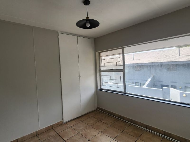 A vacant bedroom featuring tiled flooring, a built-in wardrobe, and a large window with security bars, offering a neutral canvas for potential updates.
