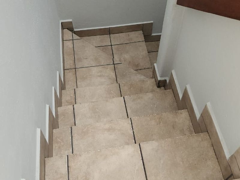 A staircase featuring neutral ceramic floor tiles and a wooden handrail, providing access between levels in the townhouse.