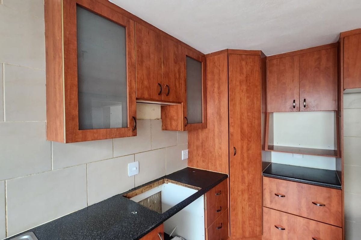 A dated kitchen area featuring wood-look cabinetry, tiled backsplash, and stone-look countertops, currently requiring a sink and appliance installation.