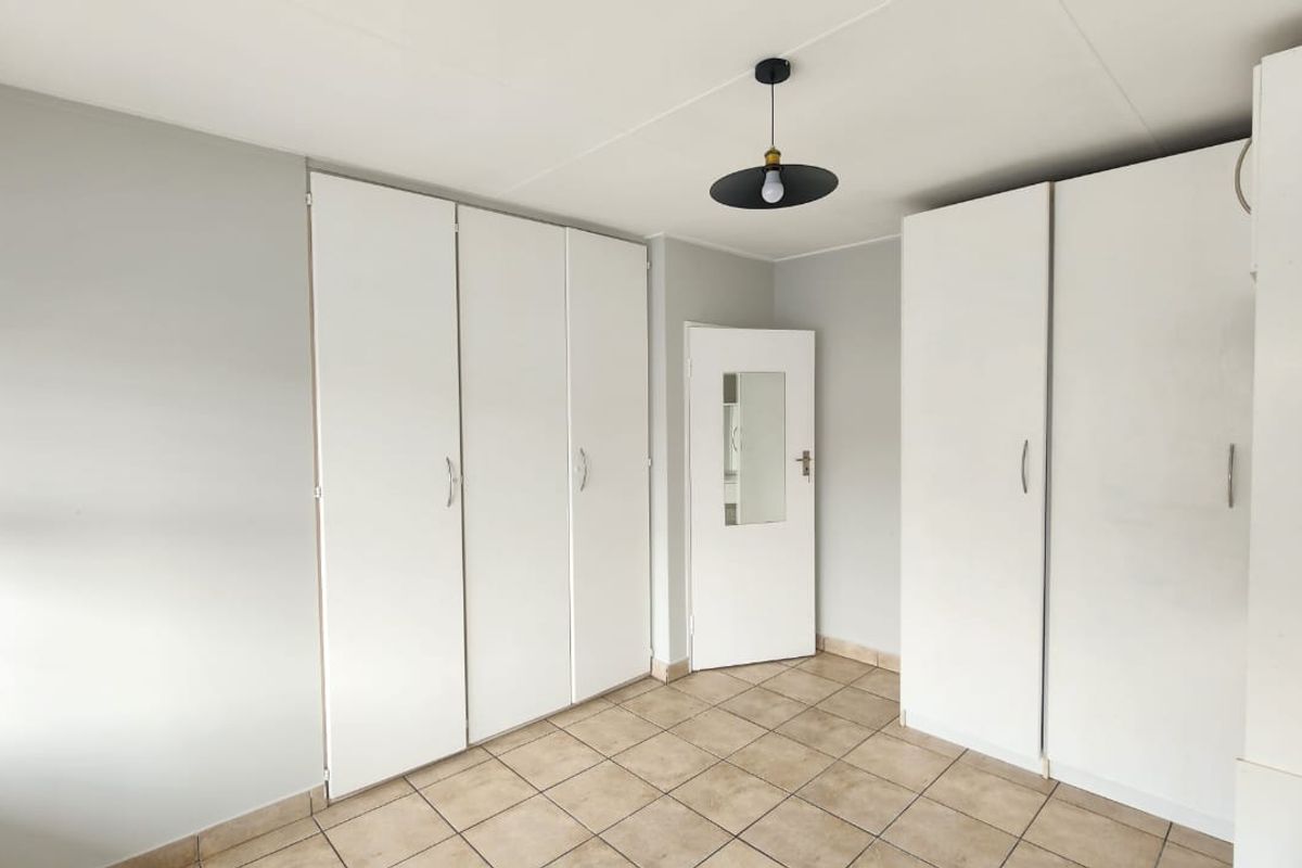 A clean, empty bedroom featuring neutral walls, tiled flooring, and extensive built-in cupboard storage.