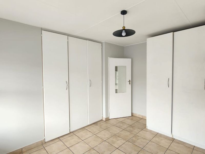 A clean, empty bedroom featuring neutral walls, tiled flooring, and extensive built-in cupboard storage.
