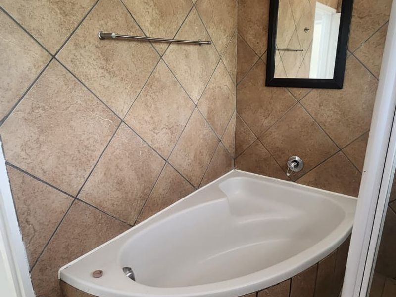 A bathroom featuring a corner bathtub with tiled surround and flooring, complemented by a shower enclosure and wall-mounted towel rail.
