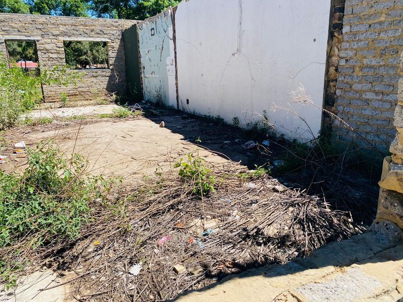 A view of a derelict structure on the property featuring exposed stone masonry walls and a concrete slab foundation in need of significant clearing.