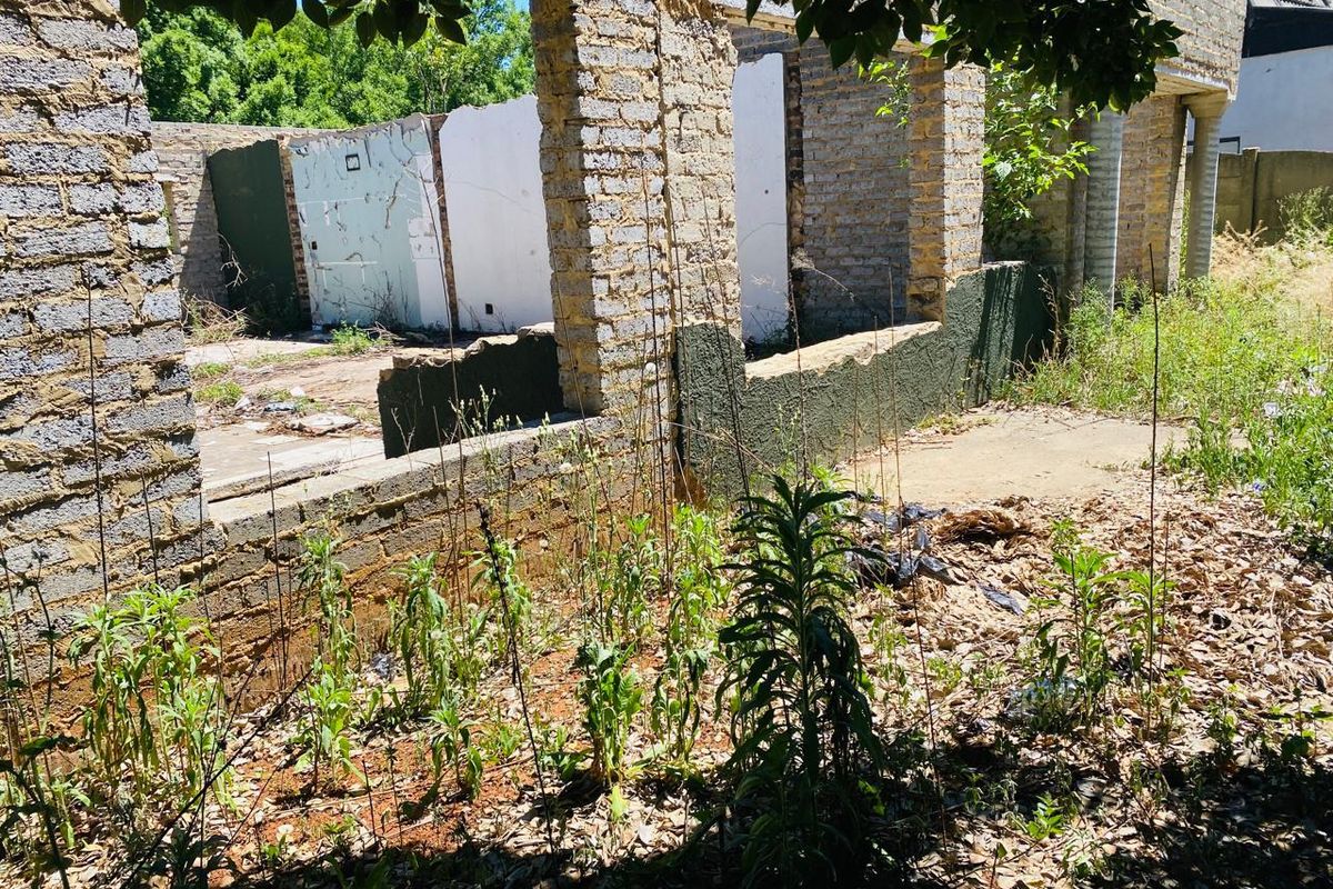 A view of a dilapidated residential structure on a vacant lot, featuring exposed brick walls and a concrete foundation requiring significant renovation or demolition.