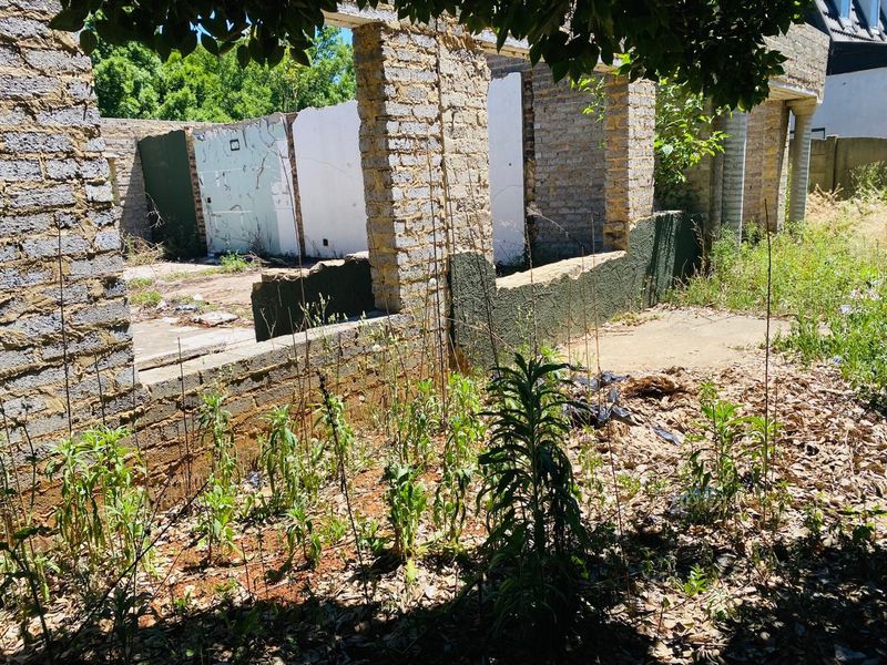 A view of a dilapidated residential structure on a vacant lot, featuring exposed brick walls and a concrete foundation requiring significant renovation or demolition.