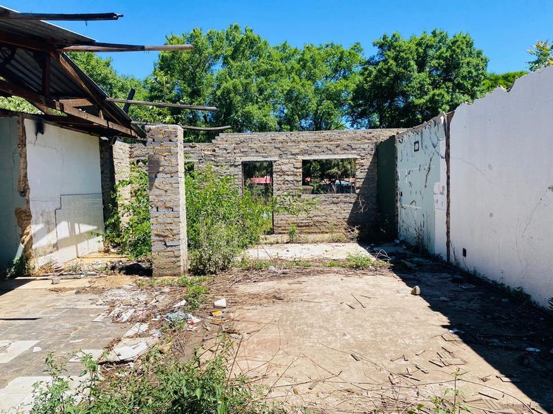 A derelict structure on a residential plot featuring collapsed roofing and severely damaged masonry walls, requiring significant clearing and reconstruction.