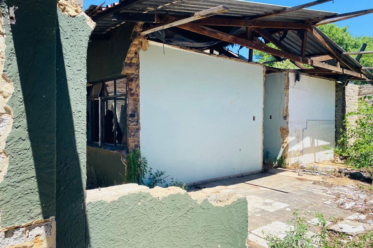 A severely dilapidated rear exterior view of a residential structure showing significant roof collapse, damaged masonry, and broken windows requiring extensive renovation or demolition.