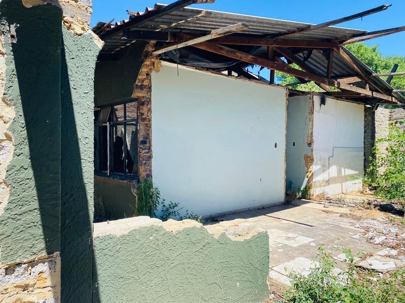 A severely dilapidated rear exterior view of a residential structure showing significant roof collapse, damaged masonry, and broken windows requiring extensive renovation or demolition.