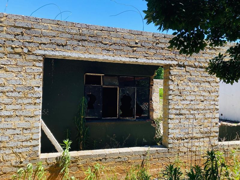 Exterior view of a residential structure showing exposed brickwork and a damaged steel window frame in need of significant repair.