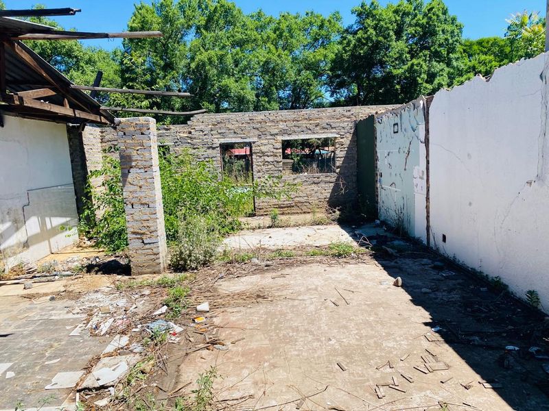 A derelict structure on a residential plot featuring exposed stone masonry walls and a collapsed roof, requiring significant clearing or demolition.