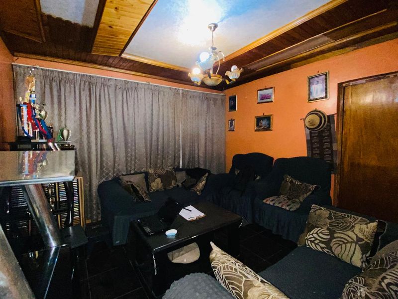 A living room featuring dark tiled flooring and a timber-paneled ceiling, currently finished with dated orange wall paint.