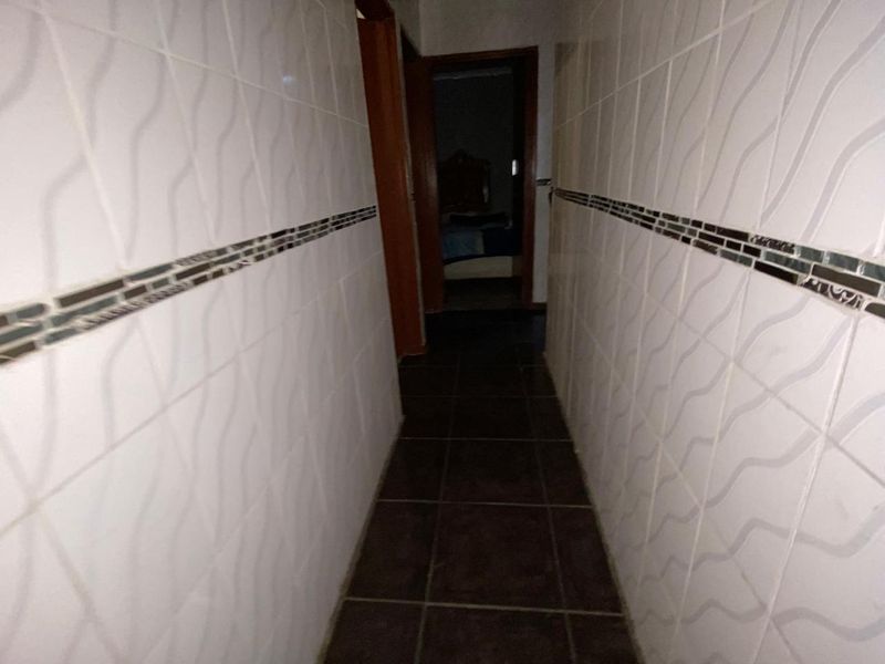 A narrow hallway featuring tiled walls with a decorative border and dark tiled flooring, leading towards an adjacent room.