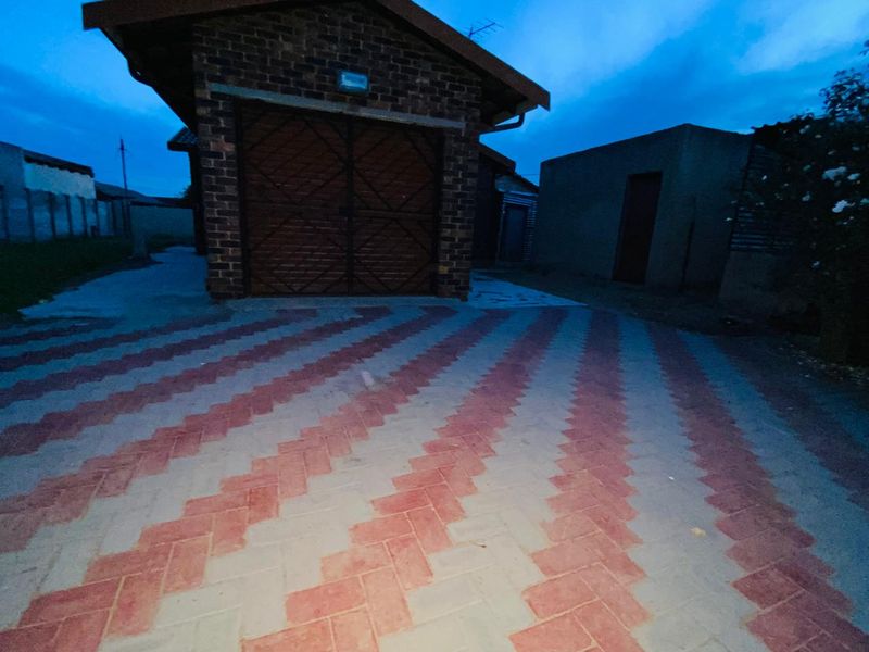Exterior view of a brick garage with a patterned paved driveway and surrounding perimeter wall at dusk.