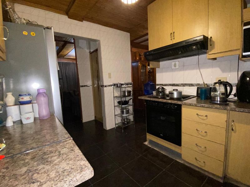 A functional kitchen featuring timber ceilings, tiled splashbacks, and built-in cabinetry with an integrated oven and hob, offering potential for modern updates.