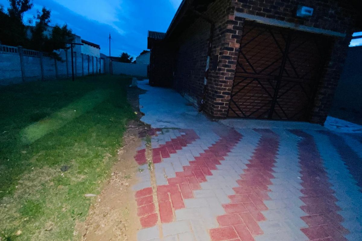 Rear exterior view of the property featuring a brick garage, paved driveway, and perimeter wall, showing signs of wear in the paving and landscaping.