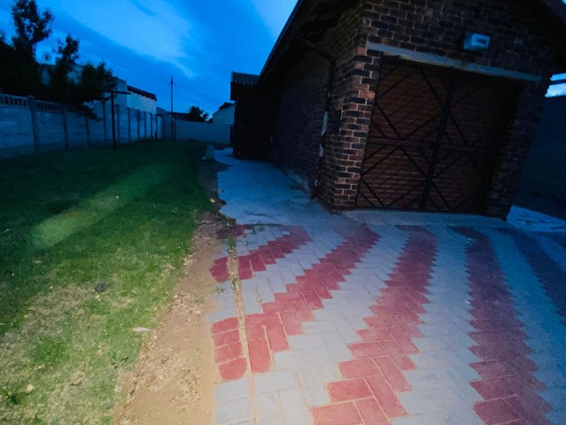 Rear exterior view of the property featuring a brick garage, paved driveway, and perimeter wall, showing signs of wear in the paving and landscaping.