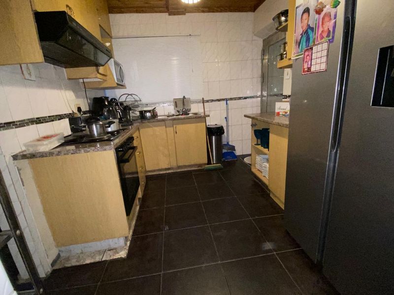 A functional kitchen featuring laminate cabinetry, built-in oven, extractor fan, and tiled surfaces, offering potential for modernization and aesthetic updates.