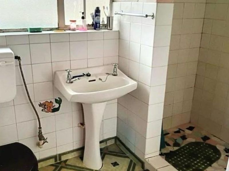 A dated bathroom featuring a pedestal basin, tiled walls, and a shower enclosure, requiring modernization of finishes and fixtures.