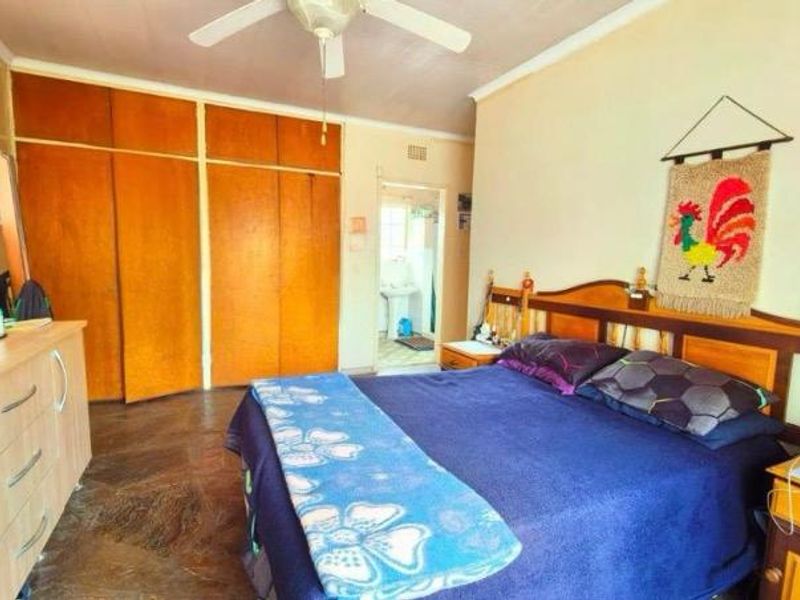 A bedroom featuring built-in wooden cupboards, a ceiling fan, and tiled flooring, with an adjacent view into a bathroom area.