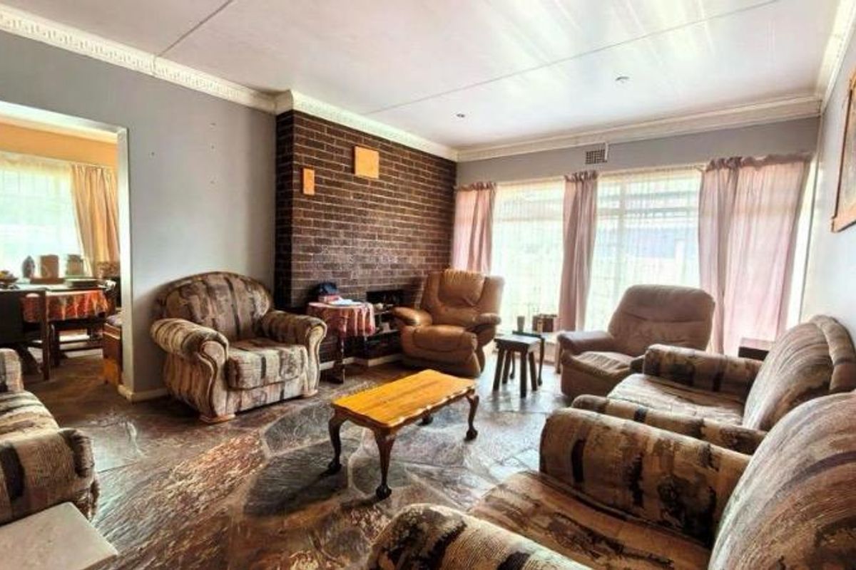 Spacious living room featuring a prominent exposed brick fireplace, unique stone flooring, and crown molding, offering a classic layout with adjacent dining area access.