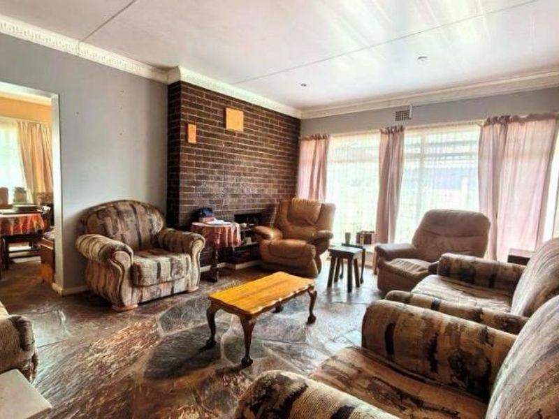 Spacious living room featuring a prominent exposed brick fireplace, unique stone flooring, and crown molding, offering a classic layout with adjacent dining area access.