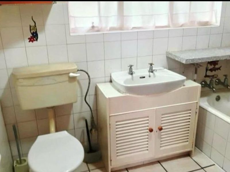 A functional bathroom featuring a built-in vanity, bathtub, and toilet, finished with classic ceramic wall and floor tiling.