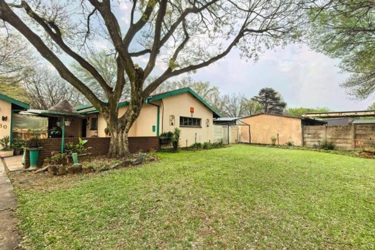Spacious rear garden featuring a large lawn, mature trees, a detached garage, and a brick boundary wall, offering potential for outdoor landscaping.